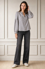 Model wearing the Aspiga Notch Neck Check Blouse in Grey/White with black jeans, full-length front view, hand raised near hair