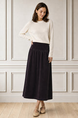 Model wearing the Aspiga Dropped Waist Baby Cord Skirt in Aubergine with a cream jumper, full-length front view