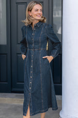 Model wearing the Aspiga A-Line Denim Midi Dress in Indigo, hands in pockets, close-up front view