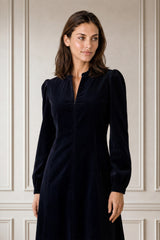 Model wearing the Aspiga Stretch Corduroy Zip Front Dress in Deep Navy, full-length front view outdoors by a doorway