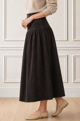 Model wearing the Aspiga Dropped Waist Baby Cord Skirt in Chocolate with a beige jumper, side view walking