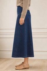 Model wearing the Aspiga Dropped Waist Denim Skirt in Indigo with a tan jumper, side view walking