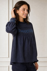 Close-up side profile of a smiling model wearing the Aspiga Seersucker Embroidered Blouse in Navy, hand in hair