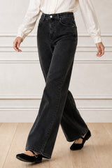 Model wearing the Aspiga Relaxed Straight Denim Jean in Black with a cream blouse, full-length front view walking