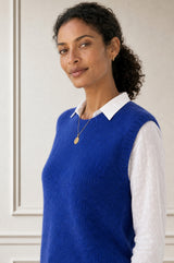 Model wearing the Aspiga Alpaca Blend Knitted Short Tank in Cobalt, a ribbed knit sweater vest layered over a white blouse, alternate view
