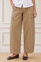 Close-up crop of a model wearing the Aspiga Matcha Trousers in Camel with a white blouse, showing the cargo pocket