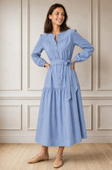 Model wearing the Aspiga Baby Cord Midi Dress in Ice Blue, a light blue corduroy belted shirt dress with long sleeves and a collar, alternate view