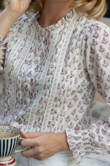 Close-up of the pintuck and lace trim detail of the Aspiga Vienna Printed Long Sleeve Blouse in Buta Pink/Cream, holding a teacup
