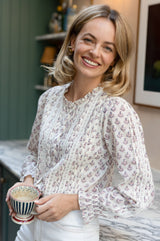 Model wearing the Aspiga Vienna Printed Long Sleeve Blouse in Buta Pink/Cream with white jeans, holding a striped teacup, smiling