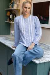 Model wearing the Aspiga Long Sleeved Striped Lace Vienna Blouse in Blue/White Stripe with jeans, seated in a kitchen, full length