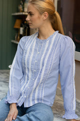 Model wearing the Aspiga Long Sleeved Striped Lace Vienna Blouse in Blue/White Stripe with jeans, seated, side profile