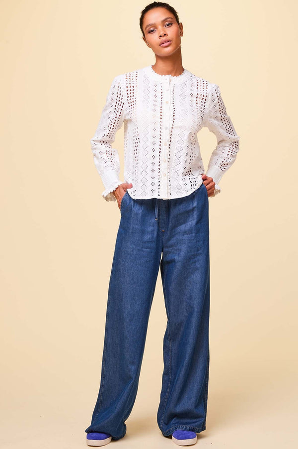Wide-leg denim trousers with relaxed fit, drawstring waist and side pockets, styled with a white broderie anglaise blouse and trainers.