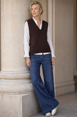Lifestyle photo of a model wearing the Aspiga Merino Wool V Neck Tank in Chocolate, a fine-knit v-neck tank layered over a blouse