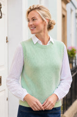 Lifestyle photo of a model wearing the Aspiga Alpaca Blend Knitted Short Tank in Light Sage, a ribbed knit sweater vest layered over a white blouse