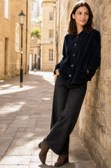 Model wearing the Aspiga Corduroy Collared Jacket in Deep Navy with dark trousers and ankle boots, leaning against a stone wall in an alleyway
