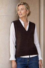 Lifestyle photo of a model wearing the Aspiga Merino Wool V Neck Tank in Chocolate, a fine-knit v-neck tank layered over a blouse