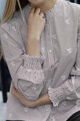 Close-up of the ruffled collar and smocked cuff of the Aspiga Cosima Embroidered Blouse in Chocolate/White