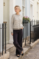 Model wearing the Aspiga Merino Wool Button Through Stripe Cardigan in Taupe/Cream with black trousers, full-length view outdoors on a street