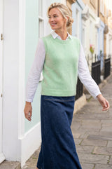 Lifestyle photo of a model wearing the Aspiga Alpaca Blend Knitted Short Tank in Light Sage, a ribbed knit sweater vest layered over a white blouse