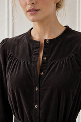 Model wearing the Aspiga Baby Cord Midi Dress in Chocolate, a chocolate brown corduroy belted shirt dress with long sleeves and a collar, alternate view