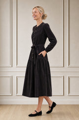 Model wearing the Aspiga Baby Cord Midi Dress in Chocolate, a chocolate brown corduroy belted shirt dress with long sleeves and a collar, alternate view