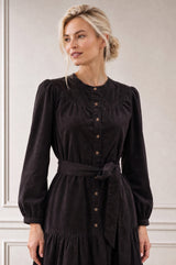 Model wearing the Aspiga Baby Cord Midi Dress in Chocolate, a chocolate brown corduroy belted shirt dress with long sleeves and a collar, alternate view