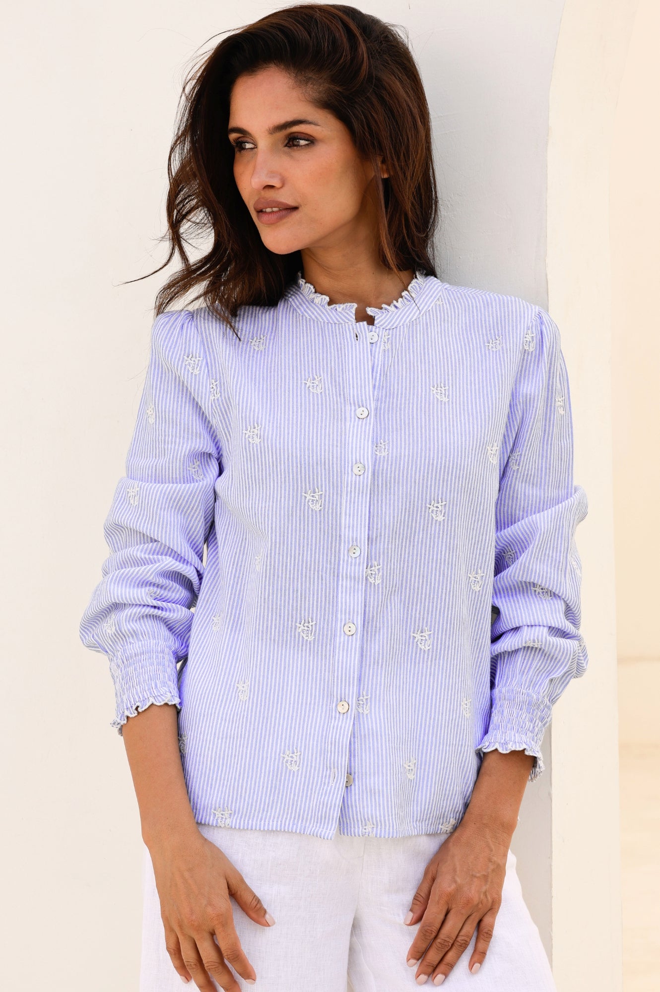 A woman wearing a blue and white long-sleeved Cosima organic cotton shirt with embroidered motifs and shirred elasticated cuffs.