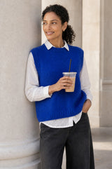 Lifestyle photo of a model wearing the Aspiga Alpaca Blend Knitted Short Tank in Cobalt, a ribbed knit sweater vest layered over a white blouse