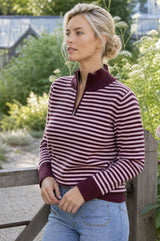 Lifestyle photo of a model wearing the Aspiga Merino Wool Stripe Quarter Zip Jumper in Burgundy/Pink, a striped quarter-zip jumper