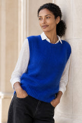 Lifestyle photo of a model wearing the Aspiga Alpaca Blend Knitted Short Tank in Cobalt, a ribbed knit sweater vest layered over a white blouse