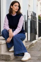 Lifestyle photo of a model wearing the Aspiga Alpaca Blend Knitted Short Tank in Navy, a ribbed knit sweater vest layered over a striped blouse