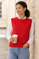 Lifestyle photo of a model wearing the Aspiga Merino Wool Knitted Short Tank in Red, a ribbed knit crew-neck sweater vest layered over a white collared blouse