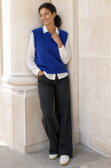 Lifestyle photo of a model wearing the Aspiga Alpaca Blend Knitted Short Tank in Cobalt, a ribbed knit sweater vest layered over a white blouse