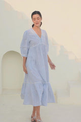Video of a woman wearing a light blue and white striped midi dress with delicate embroidery, puffed sleeves, and a tiered hem, standing against a neutral outdoor background.