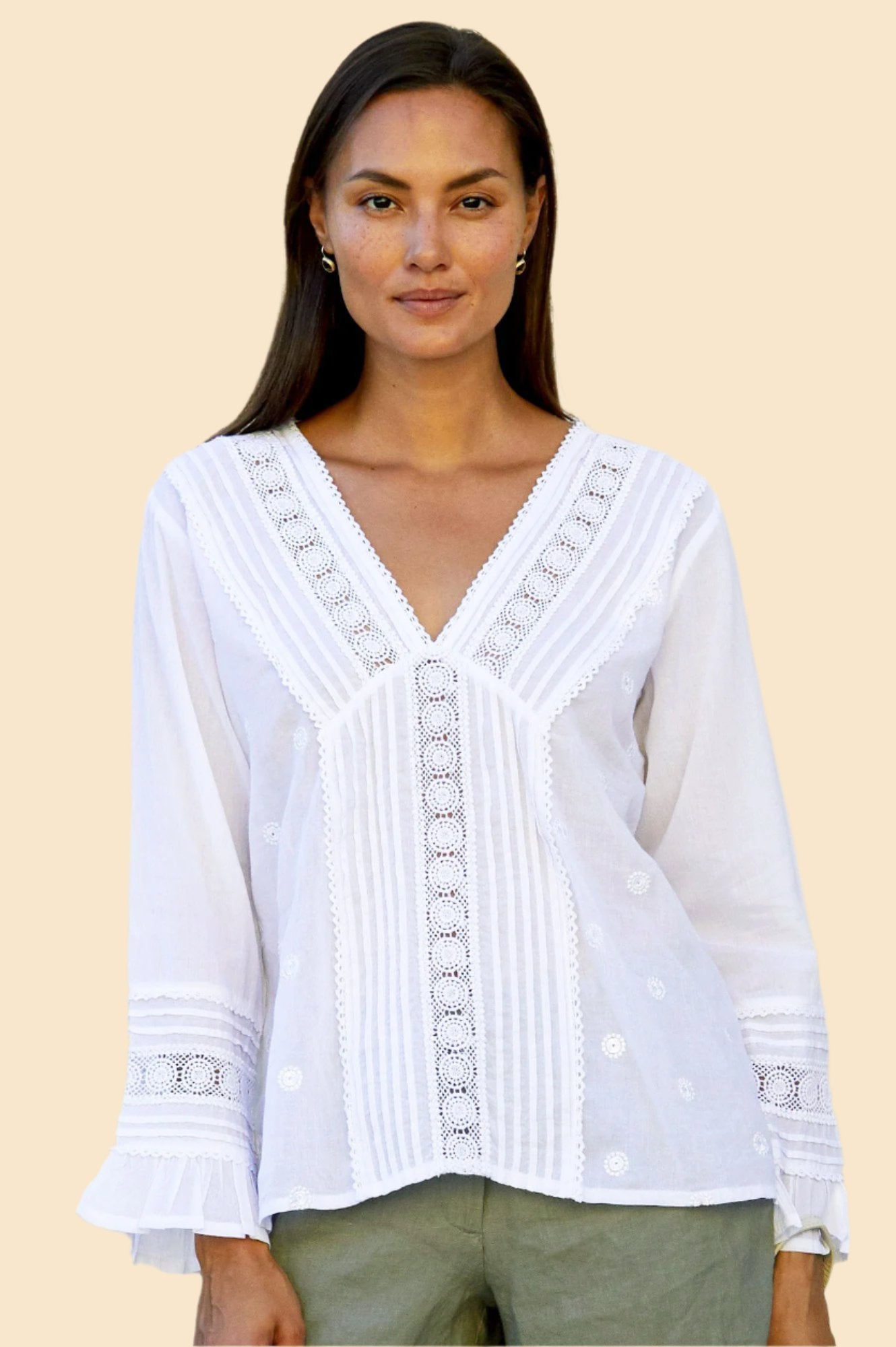A woman wearing a white V-neck blouse with full-length sleeves and delicate lace detailing, paired with green trousers.